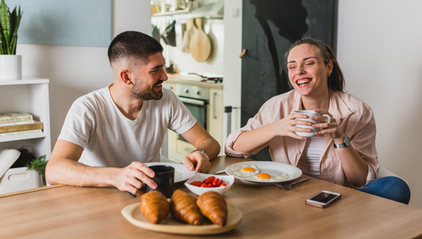 Two people having breakfast with croissants and coffee at a table.