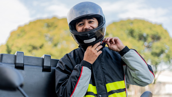 Person wearing helmet and reflective jacket adjusting helmet strap on motorcycle.